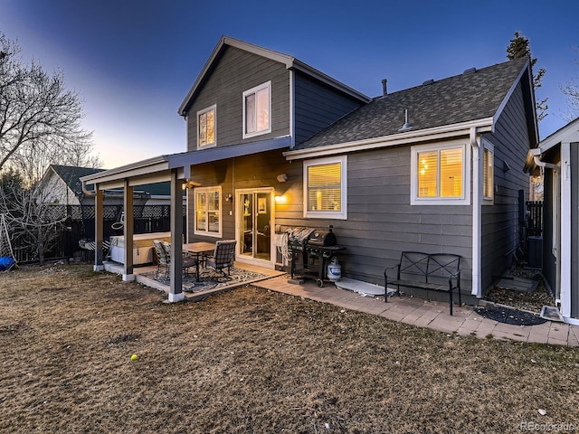 back of house at dusk featuring a fenced backyard, a patio, and roof with shingles