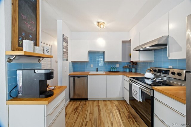 kitchen featuring stainless steel appliances, range hood, white cabinets, light wood-style flooring, and decorative backsplash