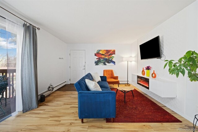 living room with light wood finished floors, a glass covered fireplace, a baseboard heating unit, baseboard heating, and healthy amount of natural light