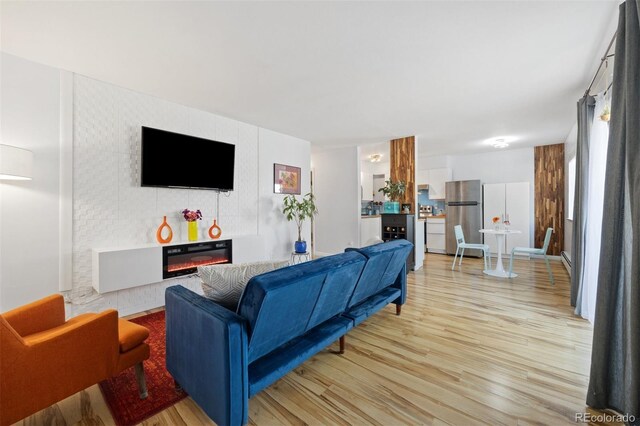 living room featuring light wood-style flooring, a glass covered fireplace, and an accent wall