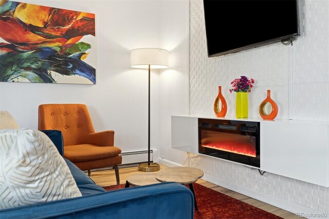 living room featuring wood finished floors, baseboard heating, and a glass covered fireplace