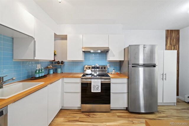 kitchen with stainless steel appliances, a sink, under cabinet range hood, white cabinetry, and tasteful backsplash