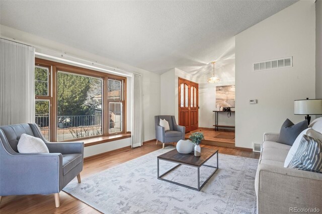 living area with visible vents, a textured ceiling, wood finished floors, and vaulted ceiling