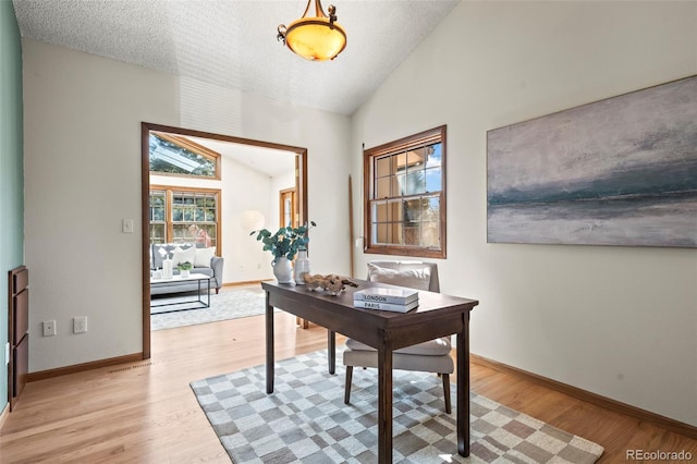 office featuring lofted ceiling, baseboards, light wood-type flooring, and a textured ceiling