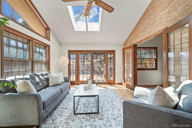 living area featuring ceiling fan, lofted ceiling with skylight, a textured ceiling, and wood finished floors