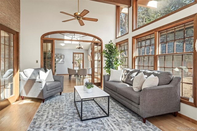 living area with ceiling fan with notable chandelier, wood finished floors, baseboards, and a towering ceiling