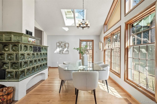 dining room featuring light wood-style flooring, lofted ceiling with skylight, and a chandelier