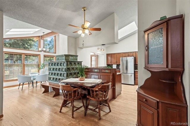 dining space featuring light wood finished floors, high vaulted ceiling, a skylight, a textured ceiling, and ceiling fan with notable chandelier