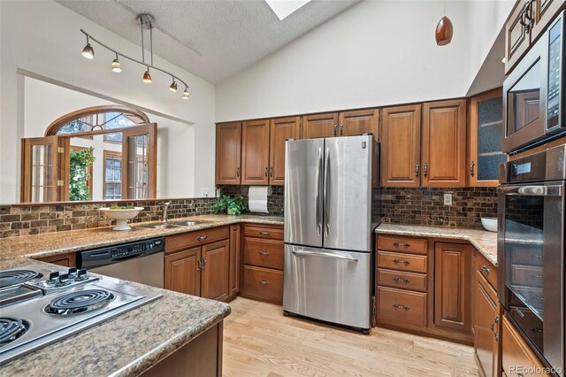 kitchen with light wood finished floors, lofted ceiling with skylight, brown cabinetry, stainless steel appliances, and a sink