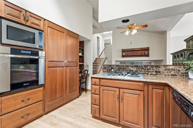 kitchen with lofted ceiling, brown cabinetry, light wood-type flooring, and stainless steel appliances