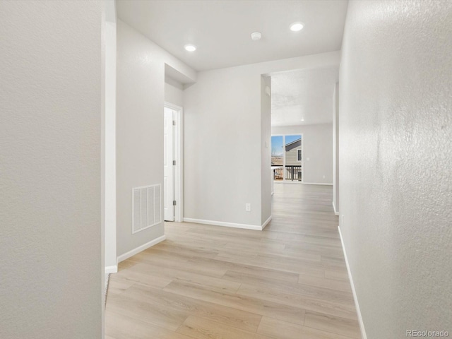 corridor featuring a textured wall, recessed lighting, visible vents, baseboards, and light wood finished floors