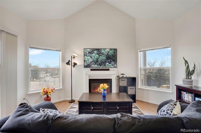 living room featuring lofted ceiling, a glass covered fireplace, light wood finished floors, and baseboards