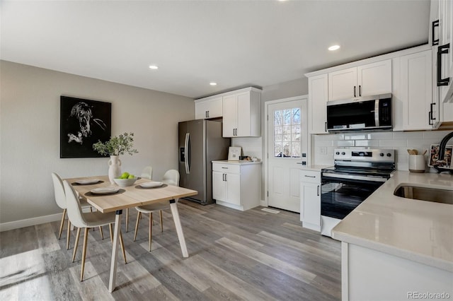 kitchen with tasteful backsplash, white cabinets, light hardwood / wood-style floors, and appliances with stainless steel finishes