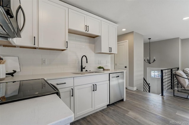 kitchen with stainless steel dishwasher, sink, light hardwood / wood-style floors, white cabinetry, and hanging light fixtures