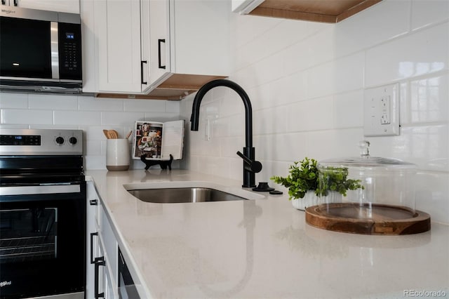 kitchen with backsplash, stainless steel appliances, white cabinetry, and sink