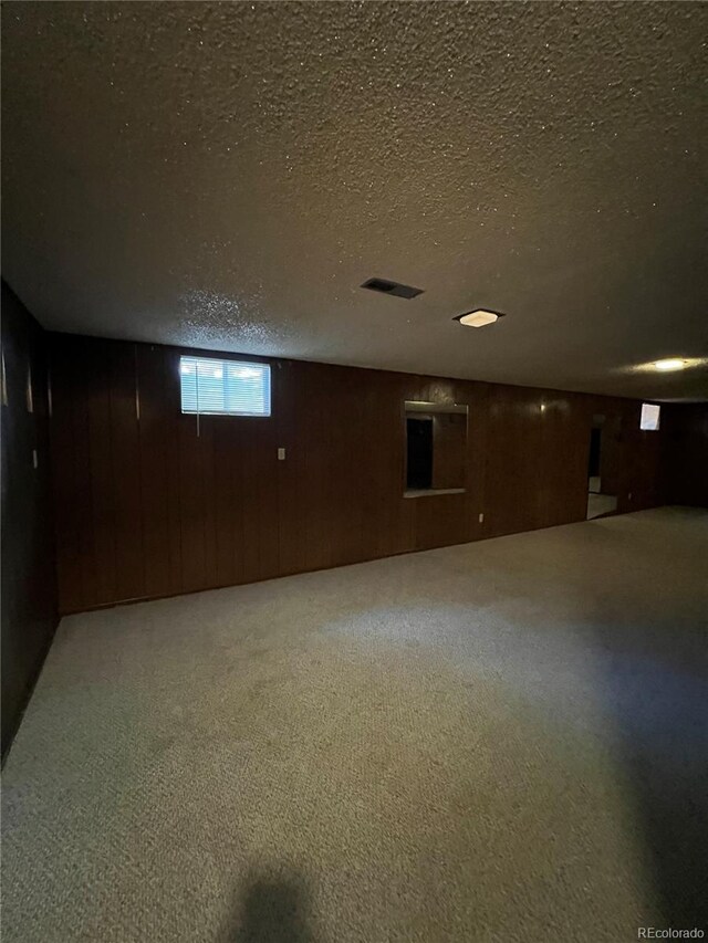 basement with wood walls, carpet floors, and a textured ceiling