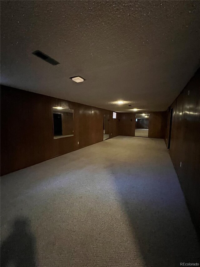 basement with a textured ceiling, carpet floors, and wooden walls