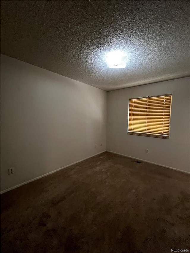 empty room featuring a textured ceiling and dark colored carpet