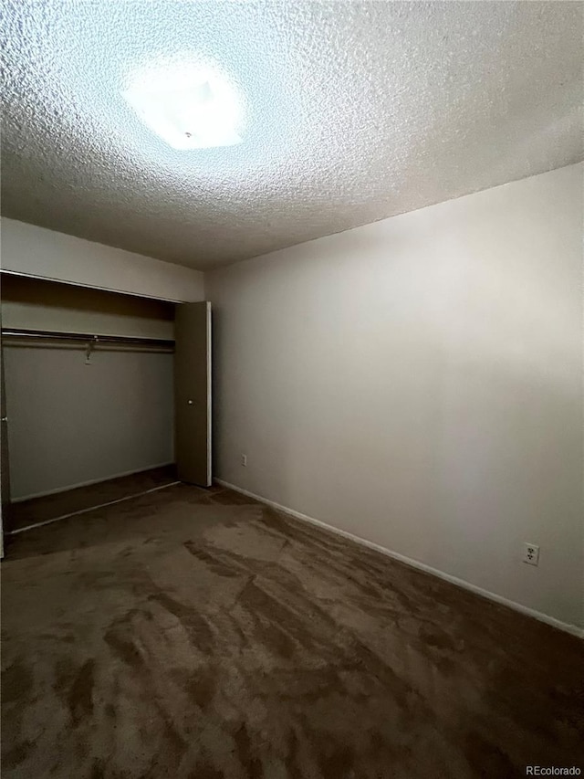 unfurnished bedroom featuring a textured ceiling, dark carpet, and a closet