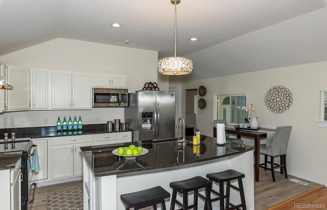 kitchen featuring hanging light fixtures, appliances with stainless steel finishes, white cabinetry, and a kitchen island with sink