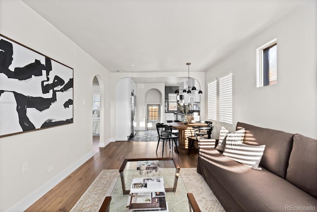 living area with baseboards, arched walkways, and wood finished floors