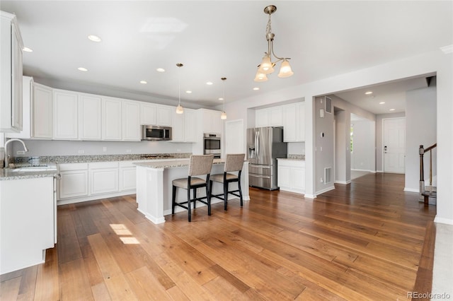 kitchen with sink, a kitchen island, light stone counters, white cabinetry, and stainless steel appliances