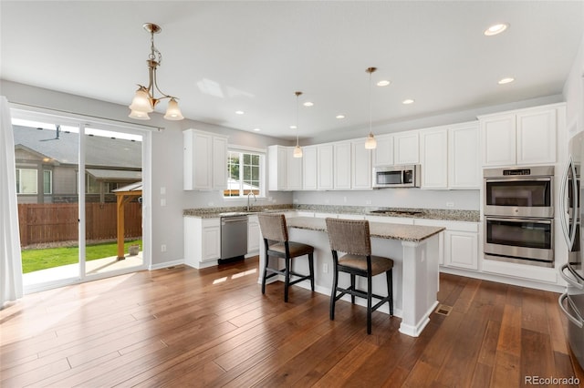 kitchen with a center island, hanging light fixtures, stainless steel appliances, light stone counters, and white cabinets