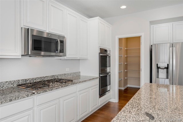 kitchen with white cabinets, light stone counters, stainless steel appliances, and dark wood-type flooring