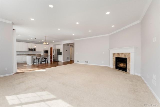 unfurnished living room featuring a tile fireplace, light carpet, an inviting chandelier, and ornamental molding