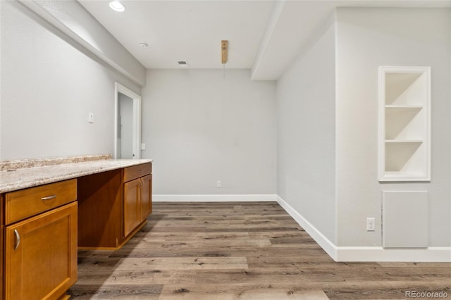 interior space featuring light hardwood / wood-style floors, built in features, light stone countertops, and built in desk