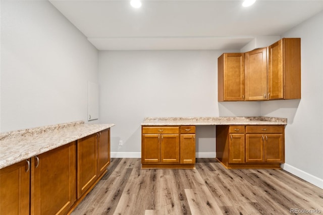 kitchen featuring light stone counters, built in desk, and light hardwood / wood-style flooring