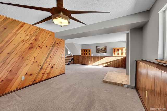 additional living space featuring light carpet, a textured ceiling, ceiling fan, and wooden walls