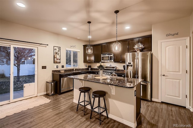 kitchen featuring appliances with stainless steel finishes, dark hardwood / wood-style flooring, dark stone counters, hanging light fixtures, and a center island