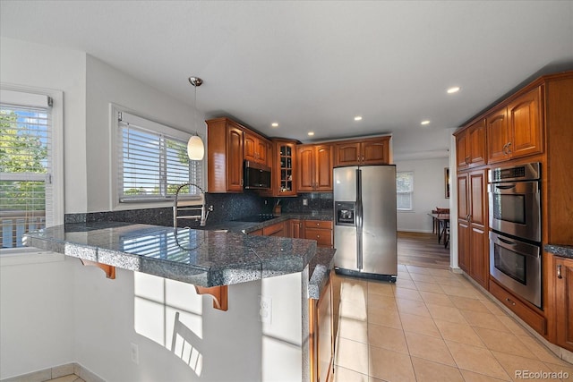 kitchen with stainless steel appliances, kitchen peninsula, light tile patterned floors, a breakfast bar, and decorative light fixtures