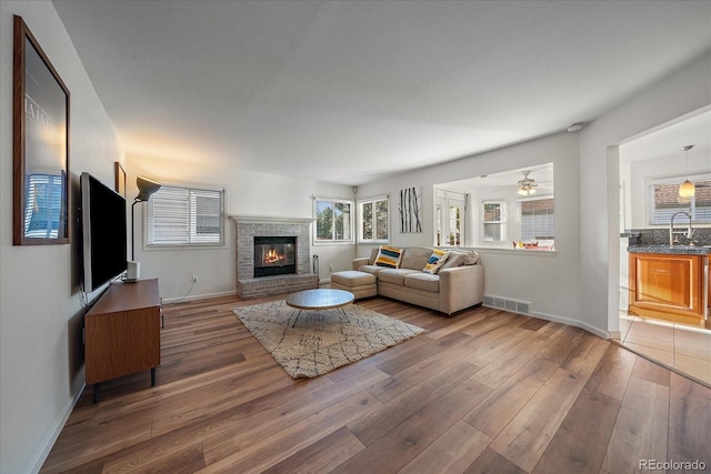 living room featuring ceiling fan, a brick fireplace, sink, and dark hardwood / wood-style floors