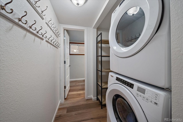 washroom featuring a textured ceiling, wood-type flooring, and stacked washer / dryer