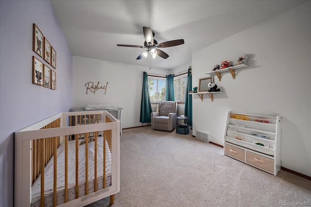 carpeted bedroom with ceiling fan and a crib