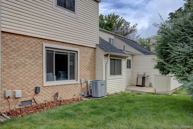 1769 S Lee St Unit B, Lakewood, CO 80232 - rear view of property featuring central AC, a yard, brick siding, roof with shingles, and a patio