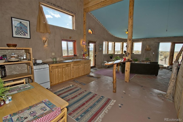 interior space featuring concrete flooring, white range with gas cooktop, sink, light brown cabinets, and a high ceiling