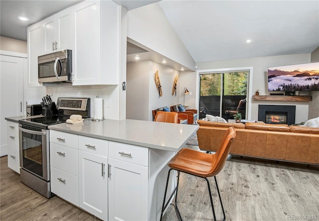 kitchen featuring stainless steel appliances, open floor plan, white cabinetry, and a kitchen bar