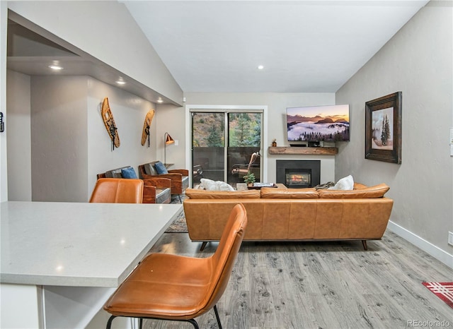 living room with baseboards, a glass covered fireplace, lofted ceiling, light wood-style floors, and recessed lighting