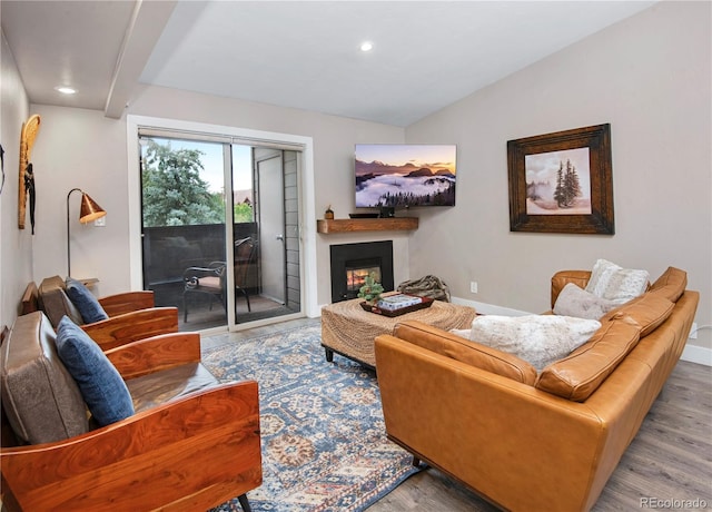 living area with lofted ceiling, recessed lighting, wood finished floors, baseboards, and a lit fireplace