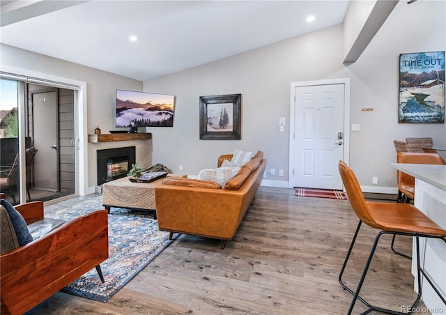 living area featuring baseboards, a glass covered fireplace, wood finished floors, vaulted ceiling, and recessed lighting