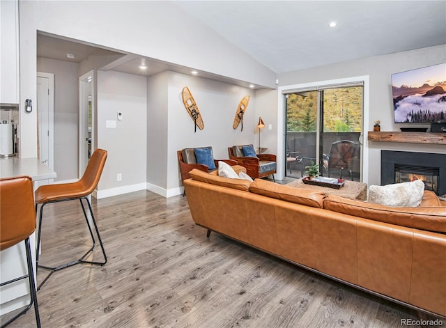 living area with light wood-style flooring, recessed lighting, baseboards, vaulted ceiling, and a glass covered fireplace