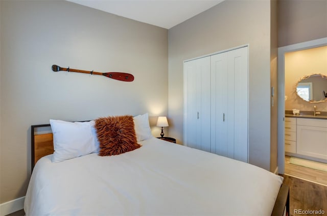 bedroom featuring connected bathroom, a sink, wood finished floors, baseboards, and a closet