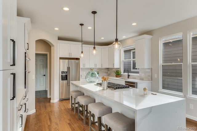 kitchen featuring stainless steel appliances, white cabinetry, a kitchen island, and decorative light fixtures