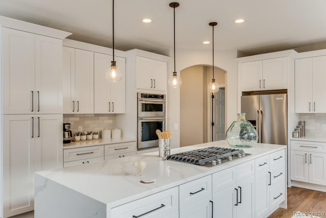 kitchen with pendant lighting, white cabinets, appliances with stainless steel finishes, a kitchen island, and tasteful backsplash