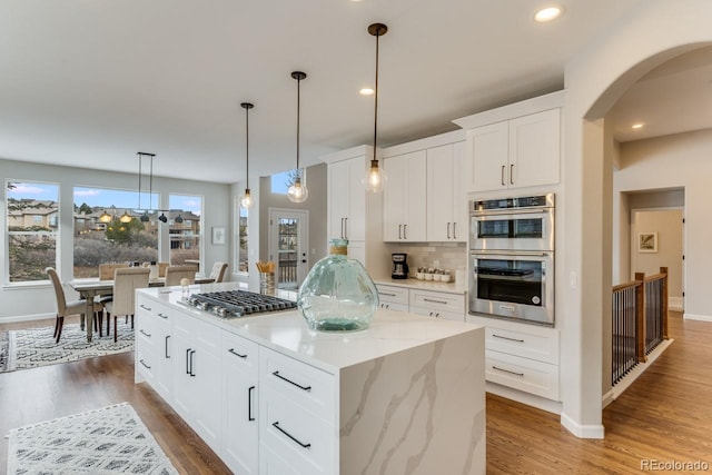 kitchen featuring a center island, hanging light fixtures, light stone countertops, appliances with stainless steel finishes, and white cabinets