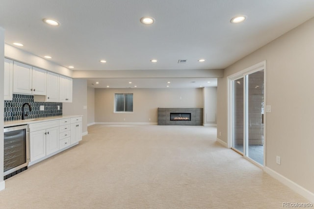 kitchen featuring wine cooler, white cabinets, light carpet, and sink