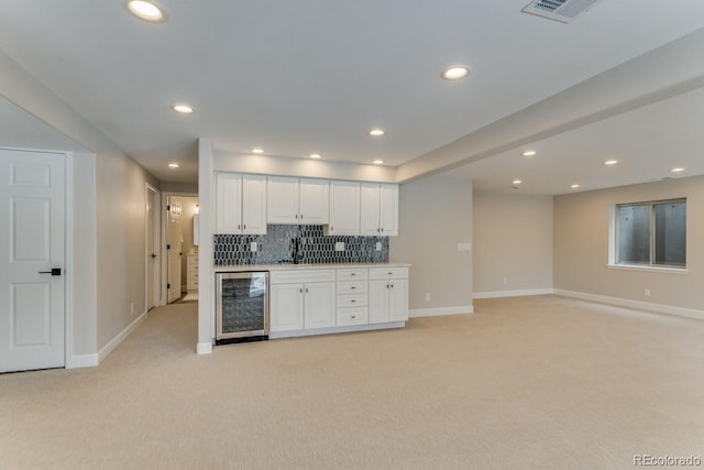 kitchen featuring light carpet, backsplash, beverage cooler, white cabinets, and sink